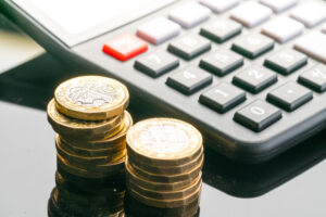 Two piles of pound coins next to a calculate to represent compensation in hospital negligence claims.